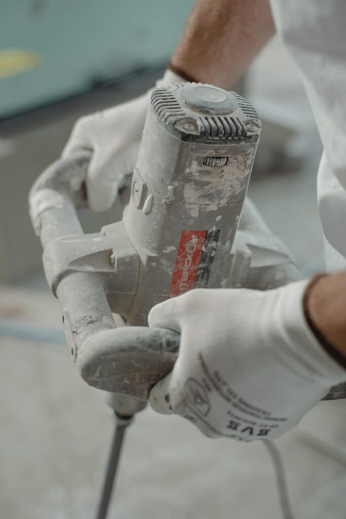 Close-up view of industrial worker's hands using a power mixer tool indoors.